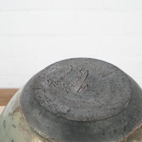 Close-up of the bottom of a ceramic bowl or vase, showing a dark gray glazed center with a light green and beige distressed rim, featuring a hand-painted signature on the base.
