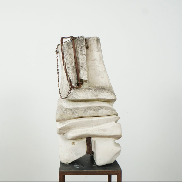 An abstract sculptural artwork made of stacked off-white stone or concrete forms with a dark brown chain-like element, displayed on a small dark pedestal against a plain light background.