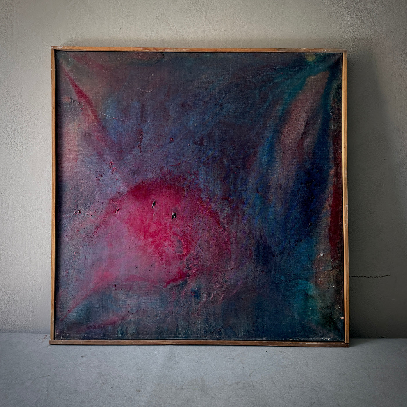 An abstract framed painting featuring a textured blend of deep blue, purple, and vibrant pink, displayed against a neutral gray wall.