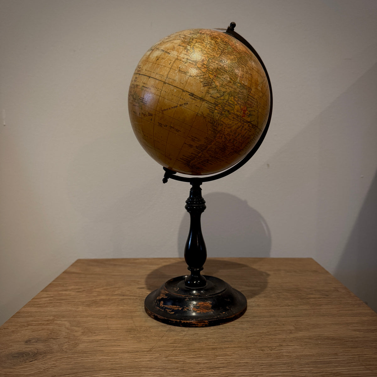 An antique-style globe with a tan map surface and a black metal stand, placed on a wooden table against a plain wall.