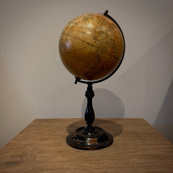 An antique-style globe with a tan map surface and a black metal stand, placed on a wooden table against a plain wall.