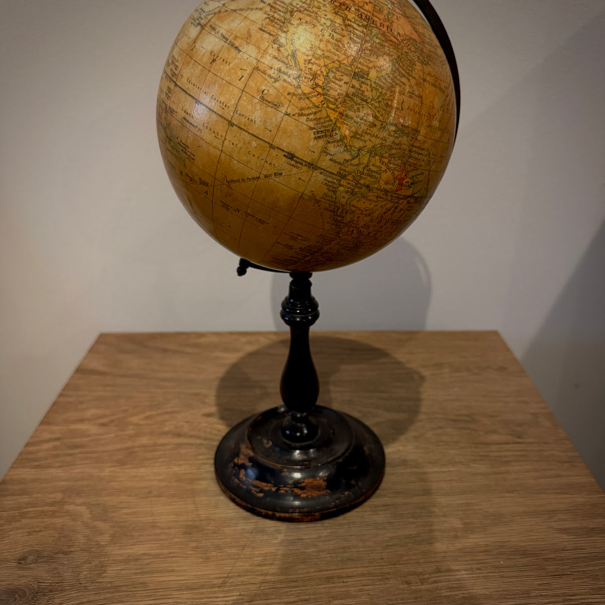 Vintage-style globe on a black stand, photographed on a wooden table against a plain light wall.