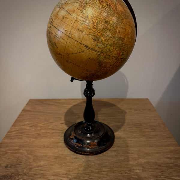 Vintage-style globe on a black stand, photographed on a wooden table against a plain light wall.