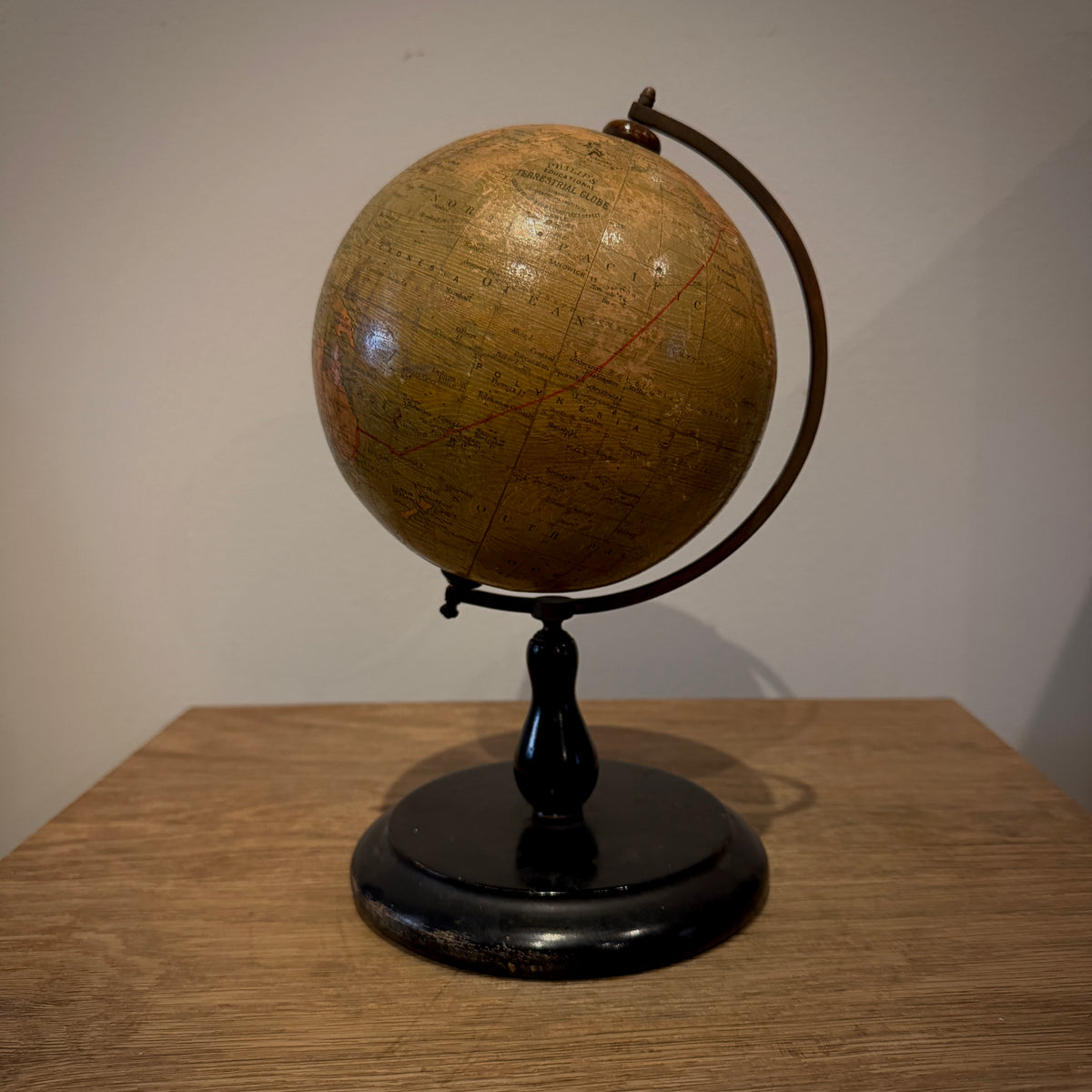 Vintage globe on a black stand, displayed on a wooden table against a plain wall.