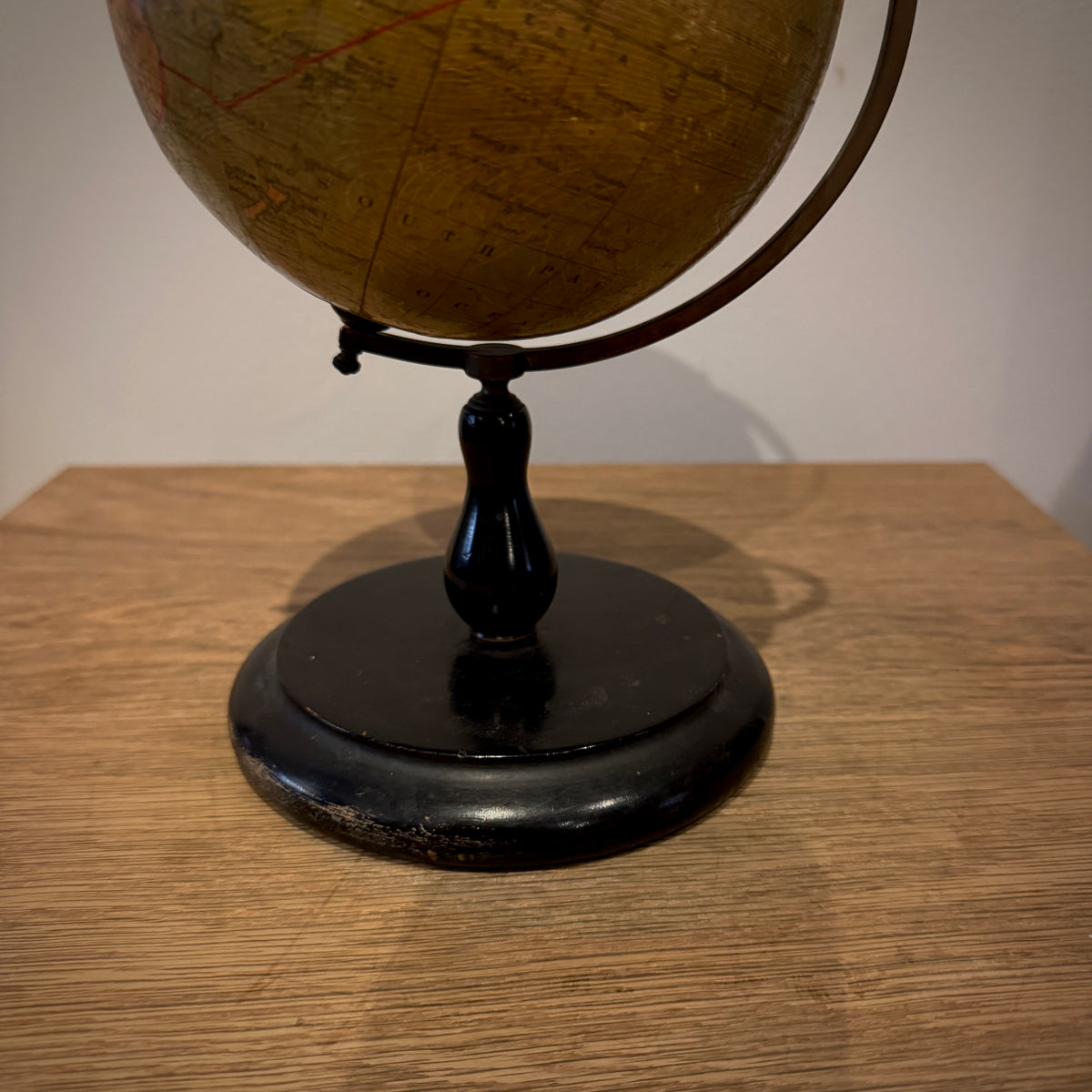 A vintage globe on a black stand placed on a wooden tabletop against a plain light wall.