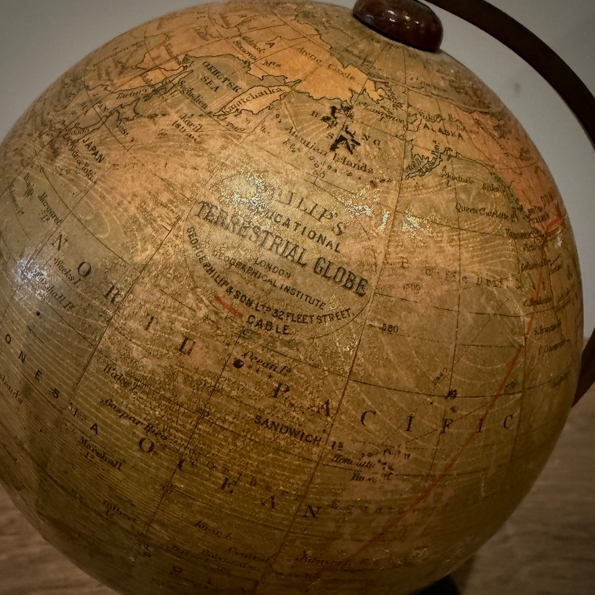 Close-up of a vintage-style terrestrial globe with an aged tan and brown map surface, showing continents, oceans, and printed text including 'Terrestrial Globe' and 'Cable.' A dark wooden stand or support is partially visible at the top and right edge.