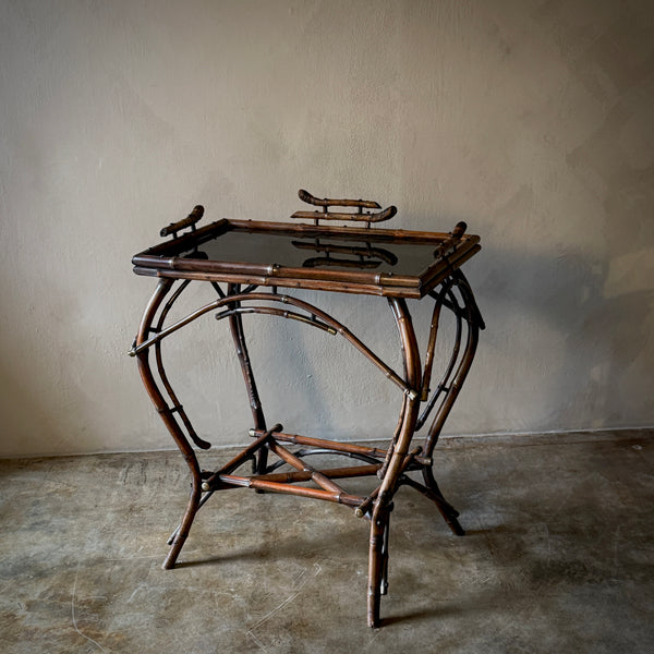A side table with a bent bamboo frame with a simple rectangular wood top against a neutral background.
