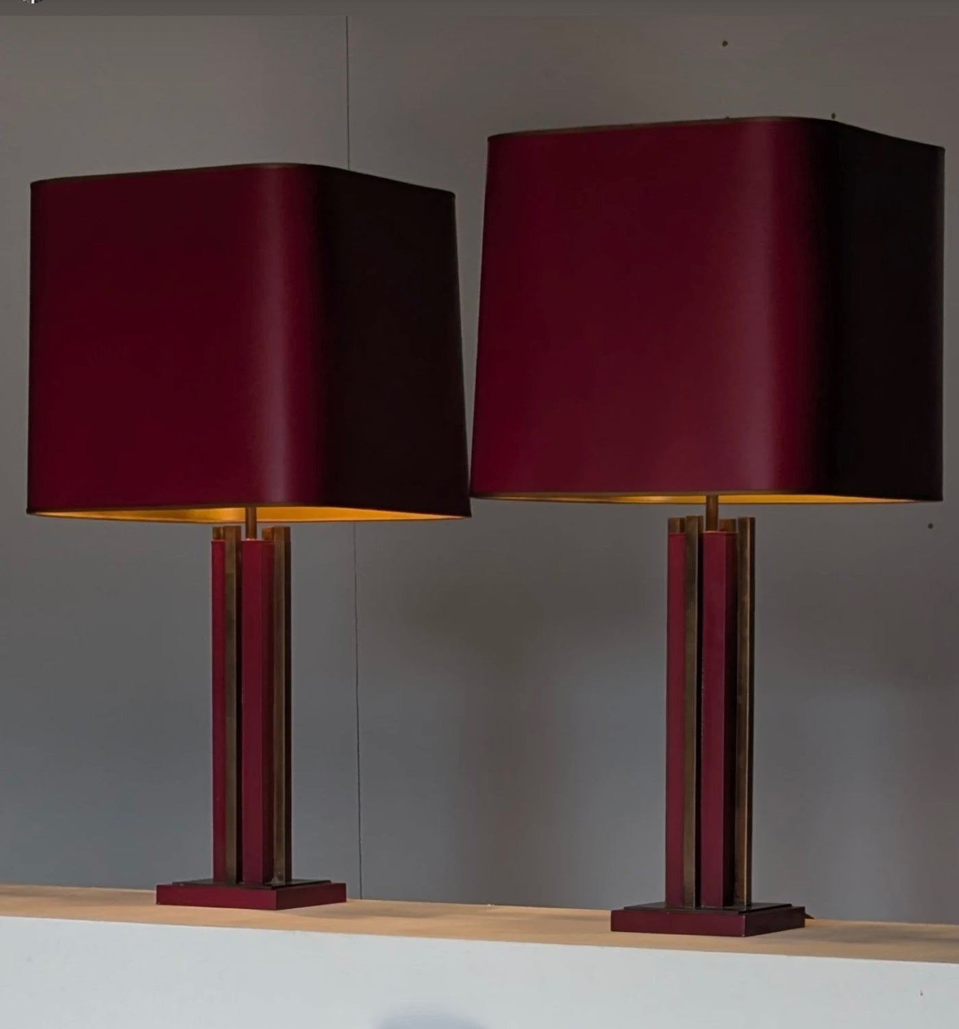 Two matching table lamps with dark burgundy shades and matching column bases, shown on a light wood surface against a neutral gray background.