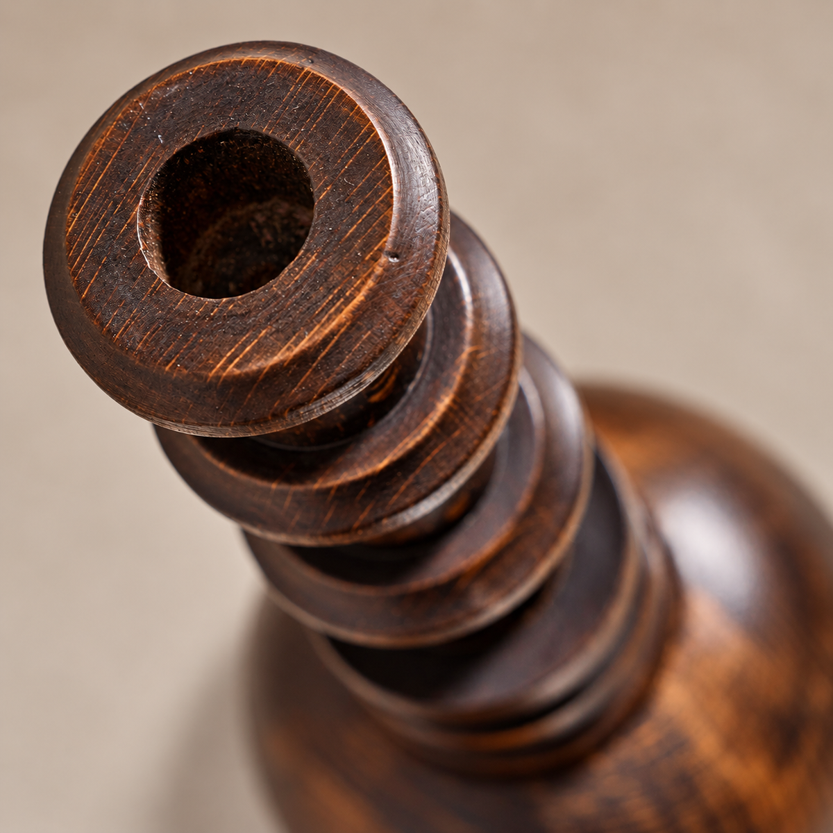 Close-up detail of a dark brown wooden object with a circular hole in the top and stacked turned sections, photographed against a soft beige background.