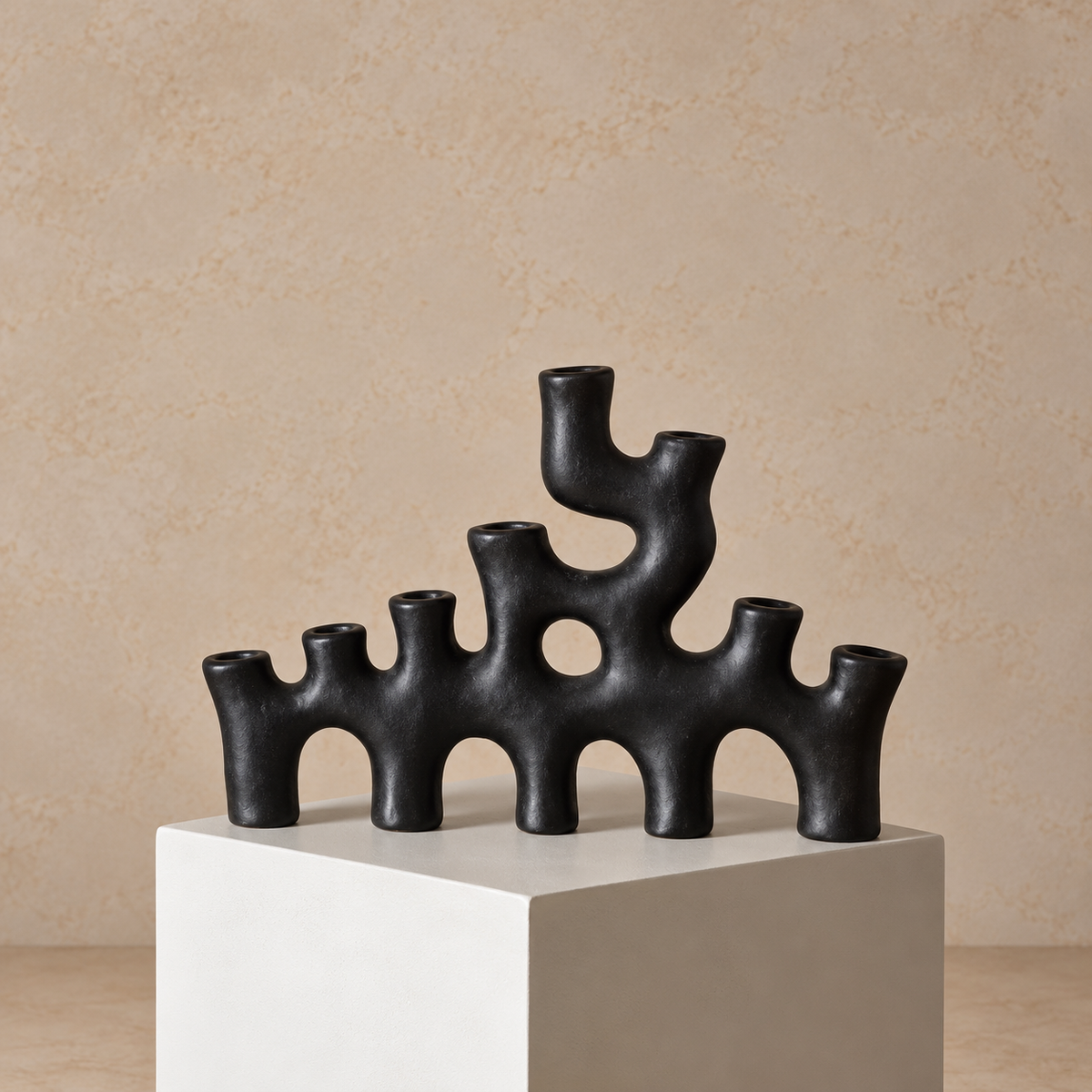 Black candelabra on a white pedestal against a beige background.