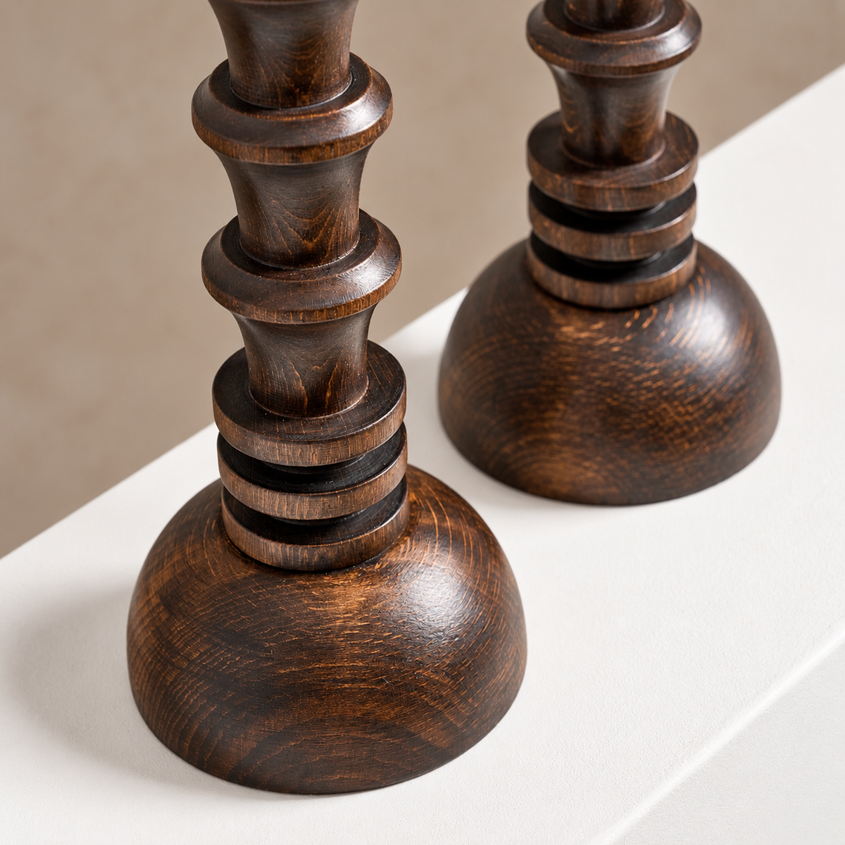 Two dark brown wooden candlesticks with a glossy finish and visible wood grain, shown on a white surface against a neutral beige background.