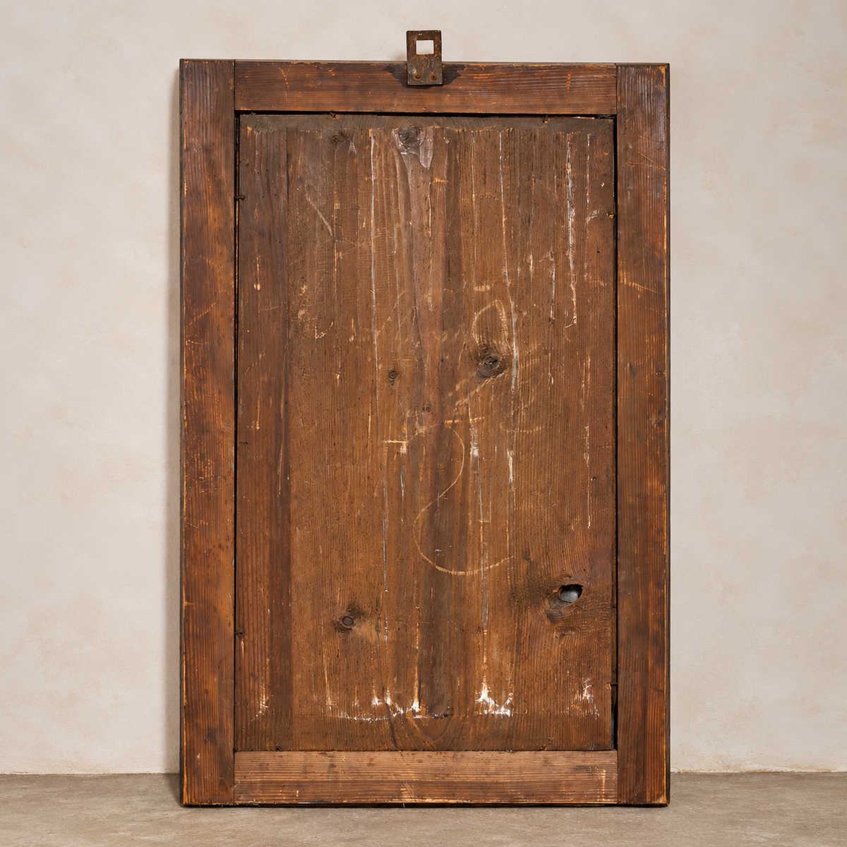 A rustic, rectangular wooden door panel with a thick frame, showing weathered brown wood grain, knots, and white chalk-like markings, set against a neutral beige wall.
