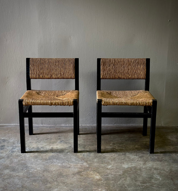 A pair of mid-century modern dining chairs with dark wooden frames and woven rush seats, set against a neutral background.