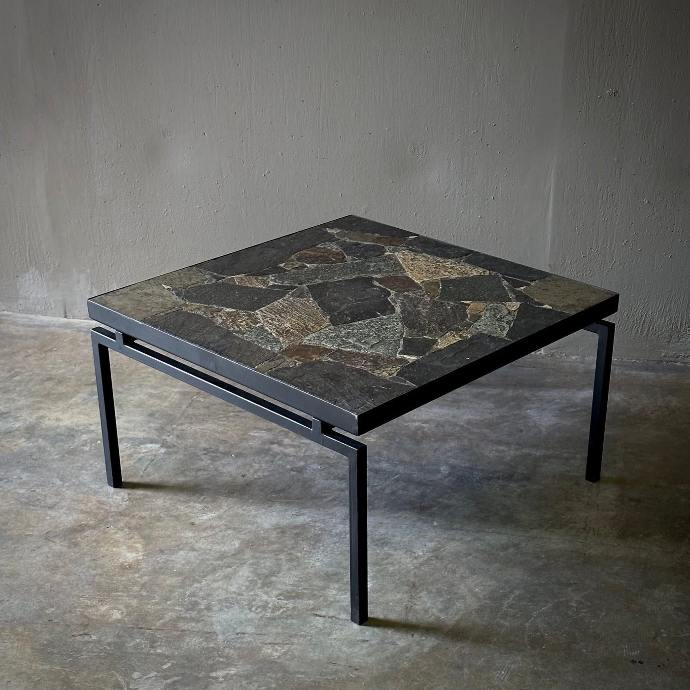 A square coffee table with a unique slate terrazzo top and a thin black metal base.