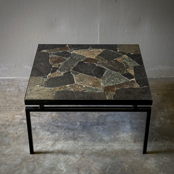 A square coffee table with a unique slate terrazzo top and a thin black metal base.