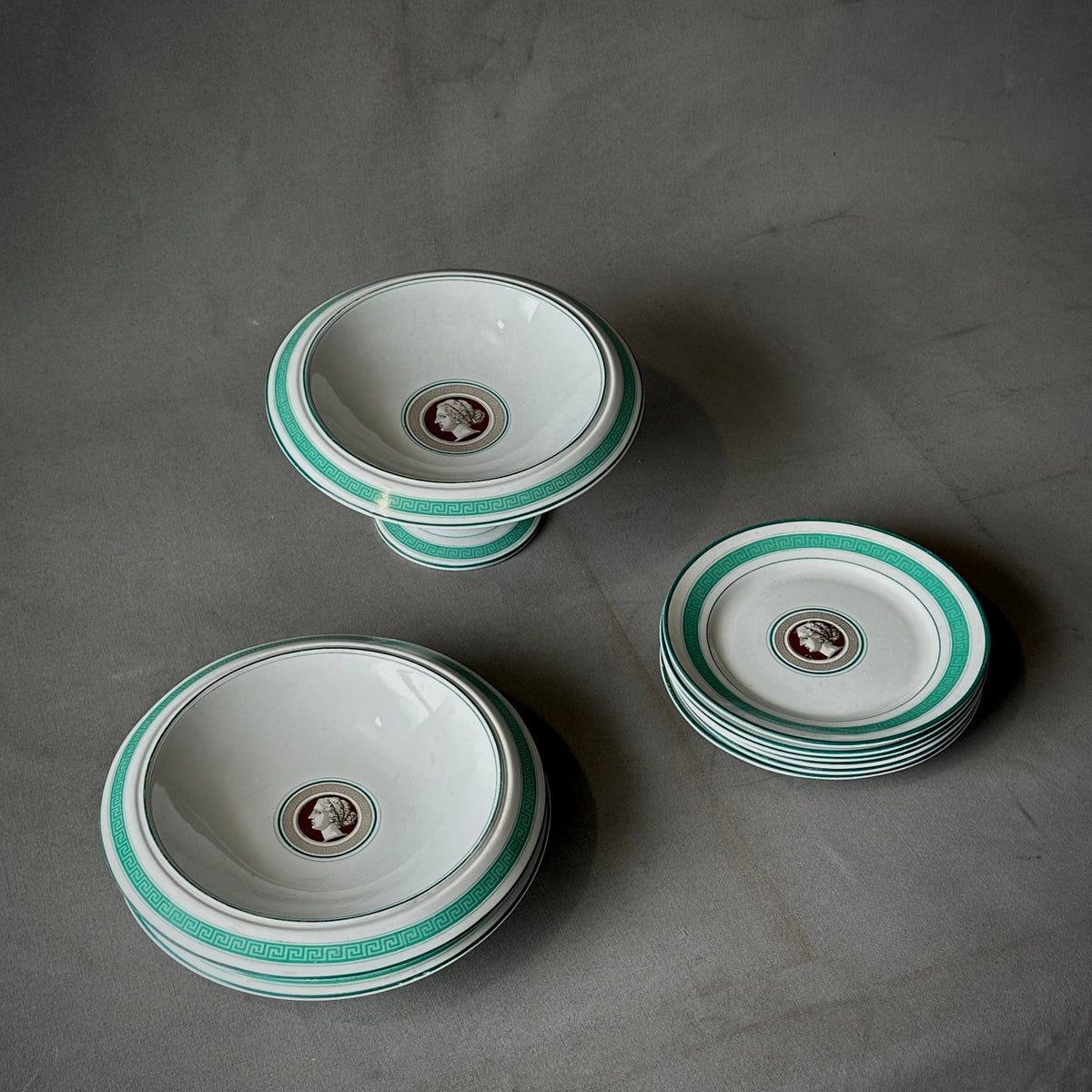 A set of porcelain dishes with a Greek key design and a medallion of a female bust in profile on each dish, featuring aquamarine trim.
