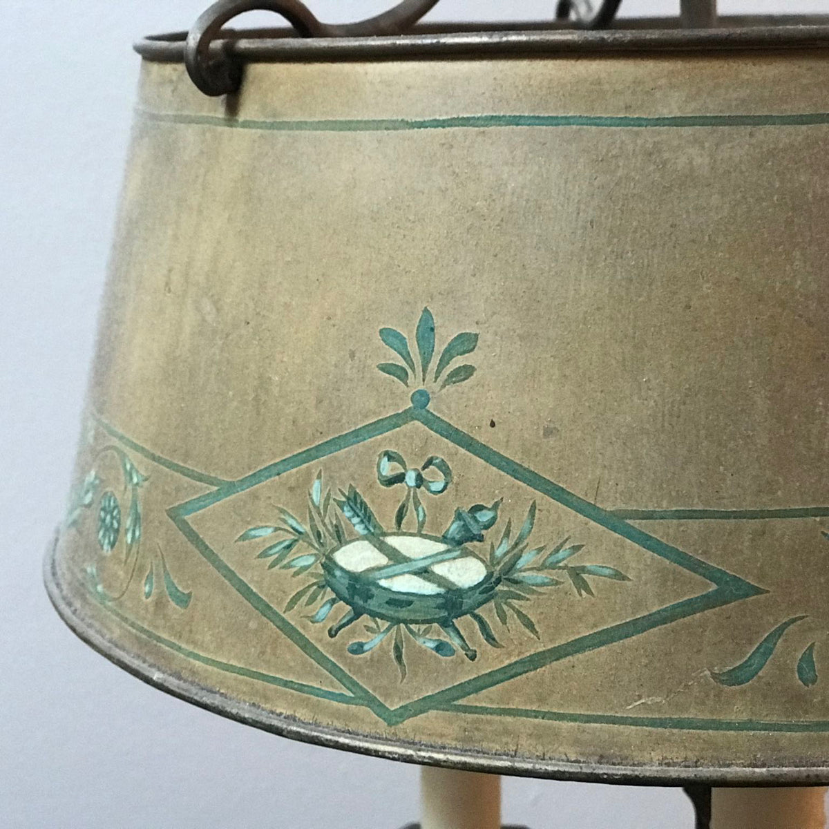 Close-up of a vintage metal lantern shade with a distressed gold/bronze finish, decorated with teal painted floral and geometric motifs, including a central basket design.