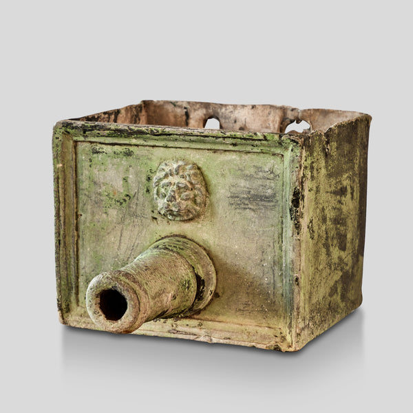 An old verdigris zinc fountain head with a classical lion's head embossed on it, showing signs of weathering and age.